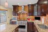 Kitchen with high end stainless steel range, wall chimney range hood, light stone countertops, decorative backsplash, and dark brown cabinetry