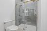Walk-in shower with clear glass enclosure and gold-toned hardware, featuring light gray subway tile