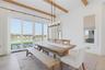 Spacious room featuring exposed wood ceiling beams, light wood-finish flooring, and a contemporary linear chandelier