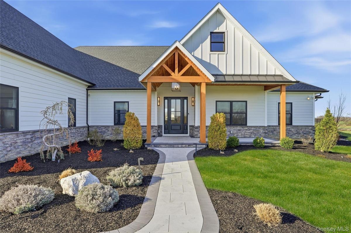 Modern farmhouse exterior featuring white siding, a dark roof, and stone facade accents