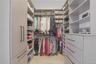 Spacious U-shaped walk-in closet featuring extensive built-in shelving, multiple hanging rods, integrated drawers with linear pulls, and wood-finish f