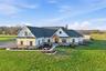 Modern farmhouse exterior featuring white board-and-batten and horizontal siding, a dark shingle roof, stone accenting, and a natural wood portico
