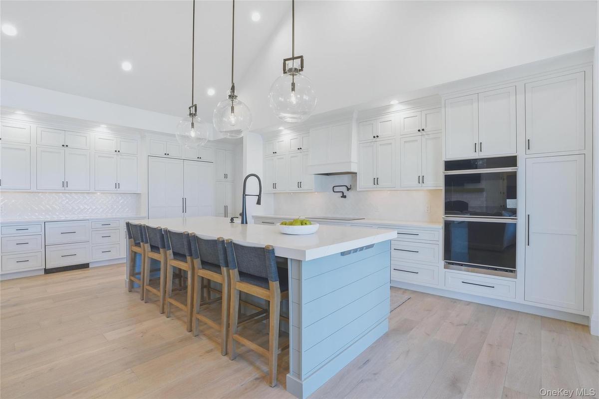 Bright kitchen featuring a large center island with seating, light wood-finish flooring, white cabinetry, integrated double ovens, and a herringbone p