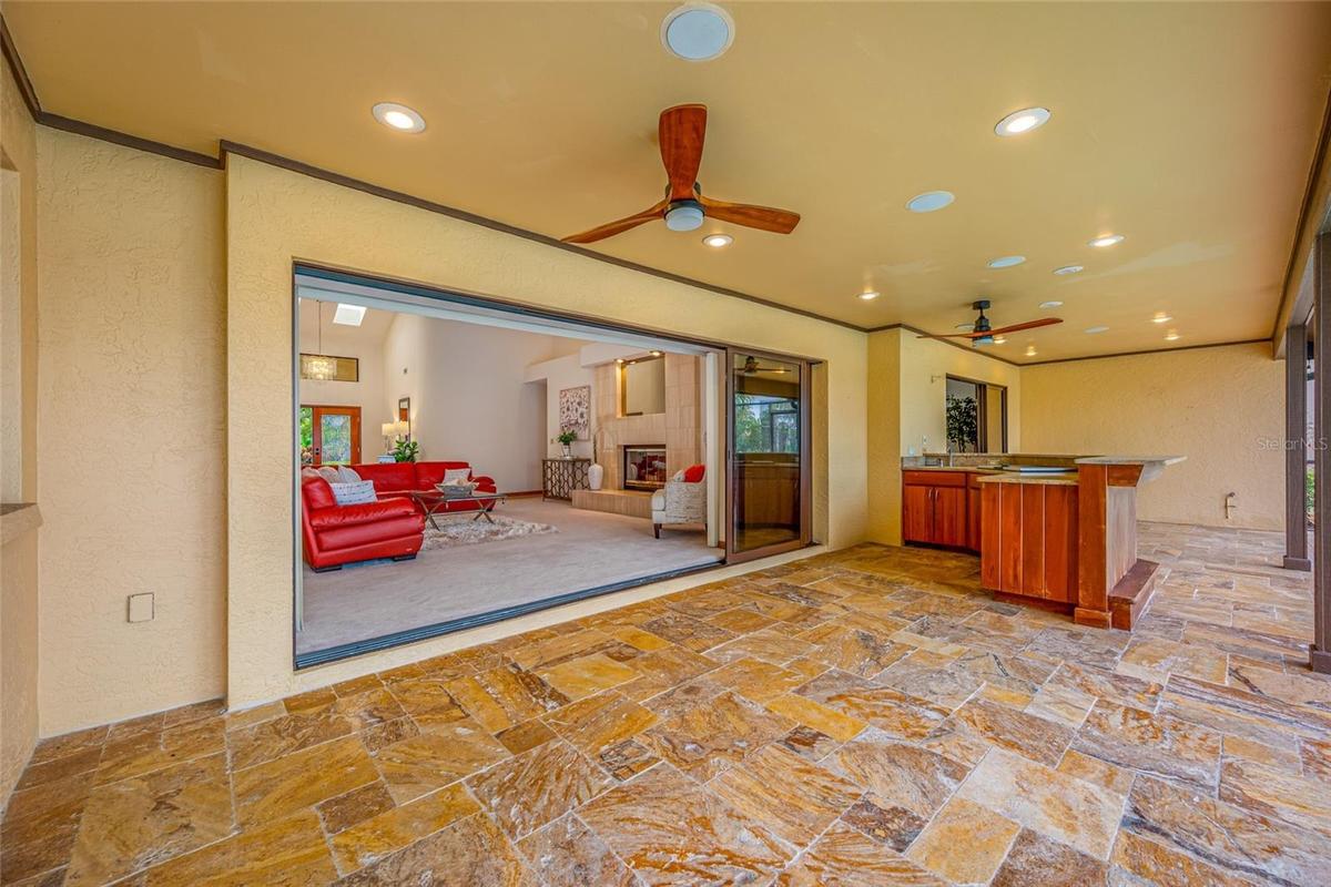Lanai view of full outdoor kitchen and grill, showing living room with triple sliders