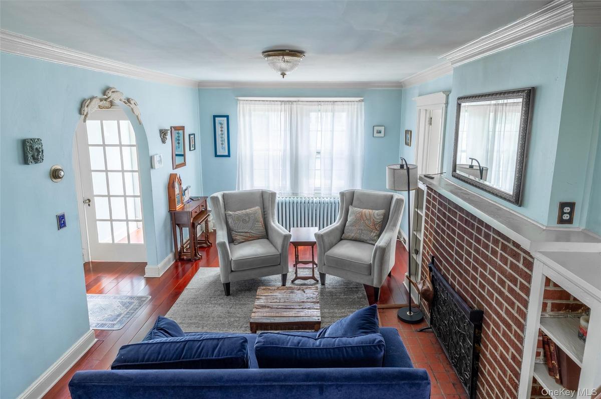Living area featuring wood-finish flooring, an arched doorway with decorative molding, and crown molding