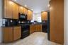 Kitchen featuring wood cabinetry, black appliances, dark countertops, and tile flooring