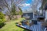 Expansive backyard featuring a manicured lawn, full privacy fencing, established trees, and a multi-level wood-finish deck