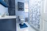 Full bathroom featuring a dark blue vanity with integrated sink, coordinating dark blue cabinetry, white square tile flooring, a white toilet, and a w