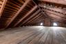 Spacious attic area featuring exposed wood beams and plank flooring