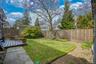 Rear yard featuring a wooden deck, stone patio, and grassy area with surrounding planting beds