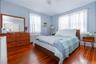 Bedroom featuring rich wood-finish flooring, light blue wall paint, and two windows providing natural illumination