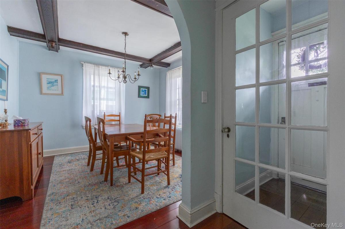 Dining area featuring exposed ceiling beams, a chandelier light fixture, wood-finish flooring, and an arched entryway