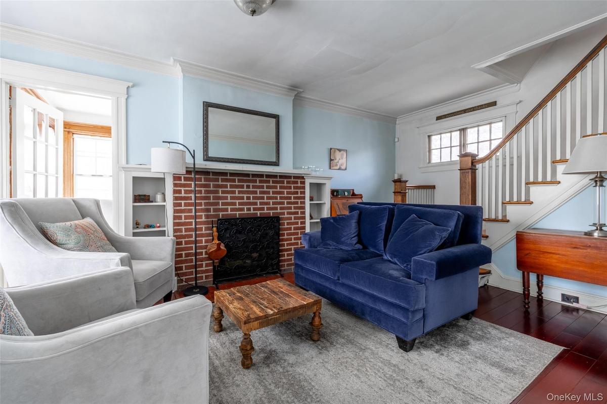 Living area featuring a brick fireplace with a white mantel and built-in shelving, hardwood flooring, and a staircase with wood newel posts and handra