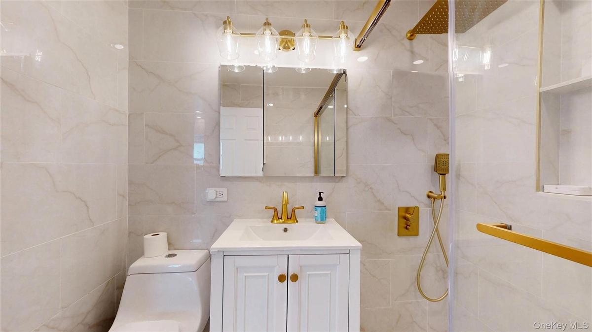 Bathroom featuring a white vanity with gold-tone hardware, a gold-tone faucet, and a mirrored medicine cabinet with integrated lighting