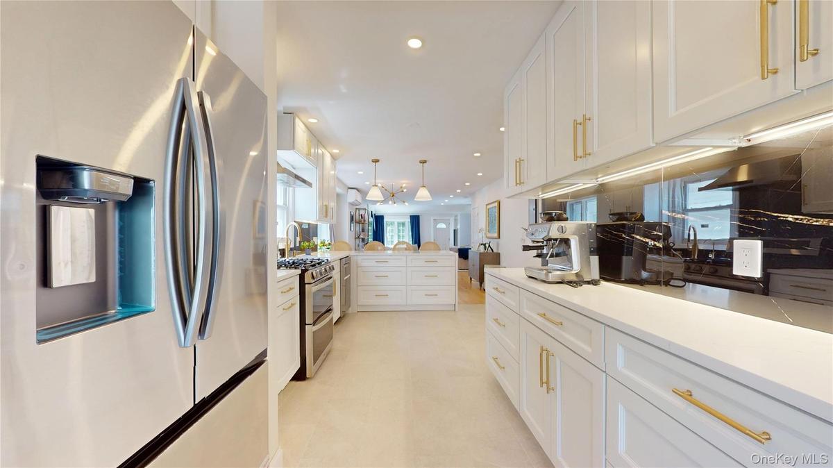 Modern kitchen featuring white cabinetry with gold-tone hardware, stainless steel appliances, and a dark stone backsplash