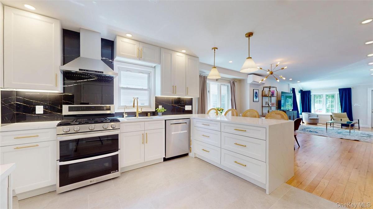 Modern kitchen featuring white cabinetry with gold-tone hardware, stainless steel appliances, and a dark stone backsplash