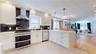 Modern kitchen featuring white cabinetry with gold-tone hardware, stainless steel appliances, and a dark stone backsplash
