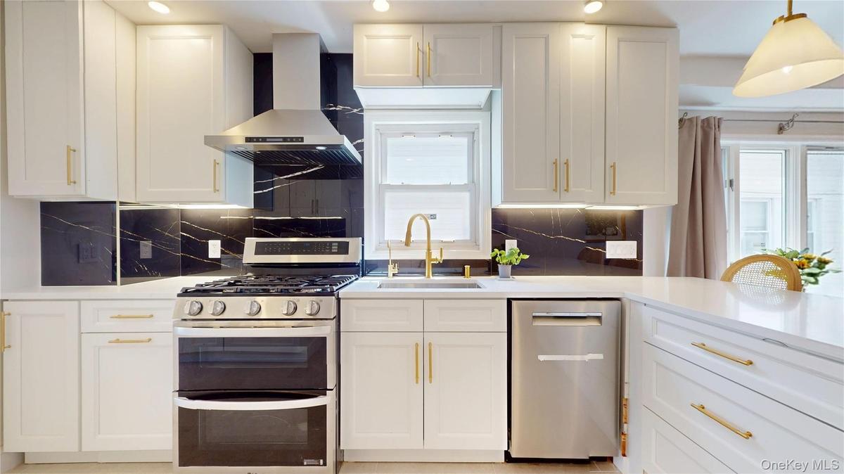 Modern kitchen featuring white cabinetry with gold-tone hardware, stainless steel appliances, and a dark stone backsplash