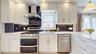 Modern kitchen featuring white cabinetry with gold-tone hardware, stainless steel appliances, and a dark stone backsplash
