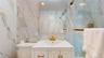 Bathroom featuring large format marble-look wall tiles, a white vanity with gold-tone hardware, a gold-tone faucet, a mirrored medicine cabinet, and a