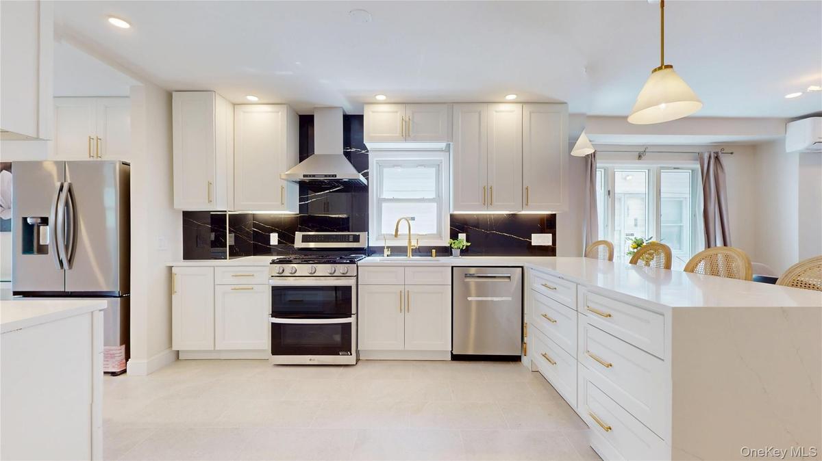 Modern kitchen featuring white cabinetry with gold-tone hardware, stainless steel appliances, and a dark stone backsplash