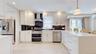 Modern kitchen featuring white cabinetry with gold-tone hardware, stainless steel appliances, and a dark stone backsplash