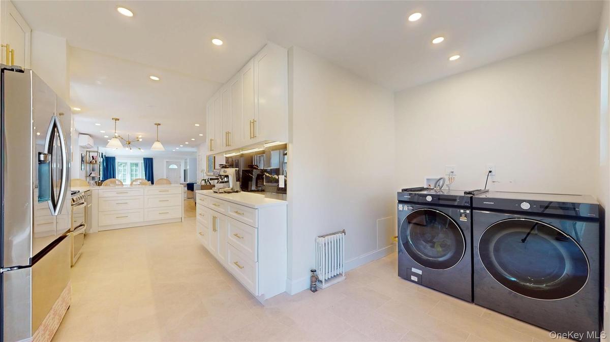 Expansive kitchen and laundry area featuring light-toned flooring, recessed lighting, and white cabinetry with gold-toned hardware