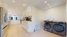 Expansive kitchen and laundry area featuring light-toned flooring, recessed lighting, and white cabinetry with gold-toned hardware