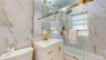 Bathroom featuring large format marble-look wall tiles, a white vanity with gold-tone hardware, a gold-tone faucet, a mirrored medicine cabinet, and a