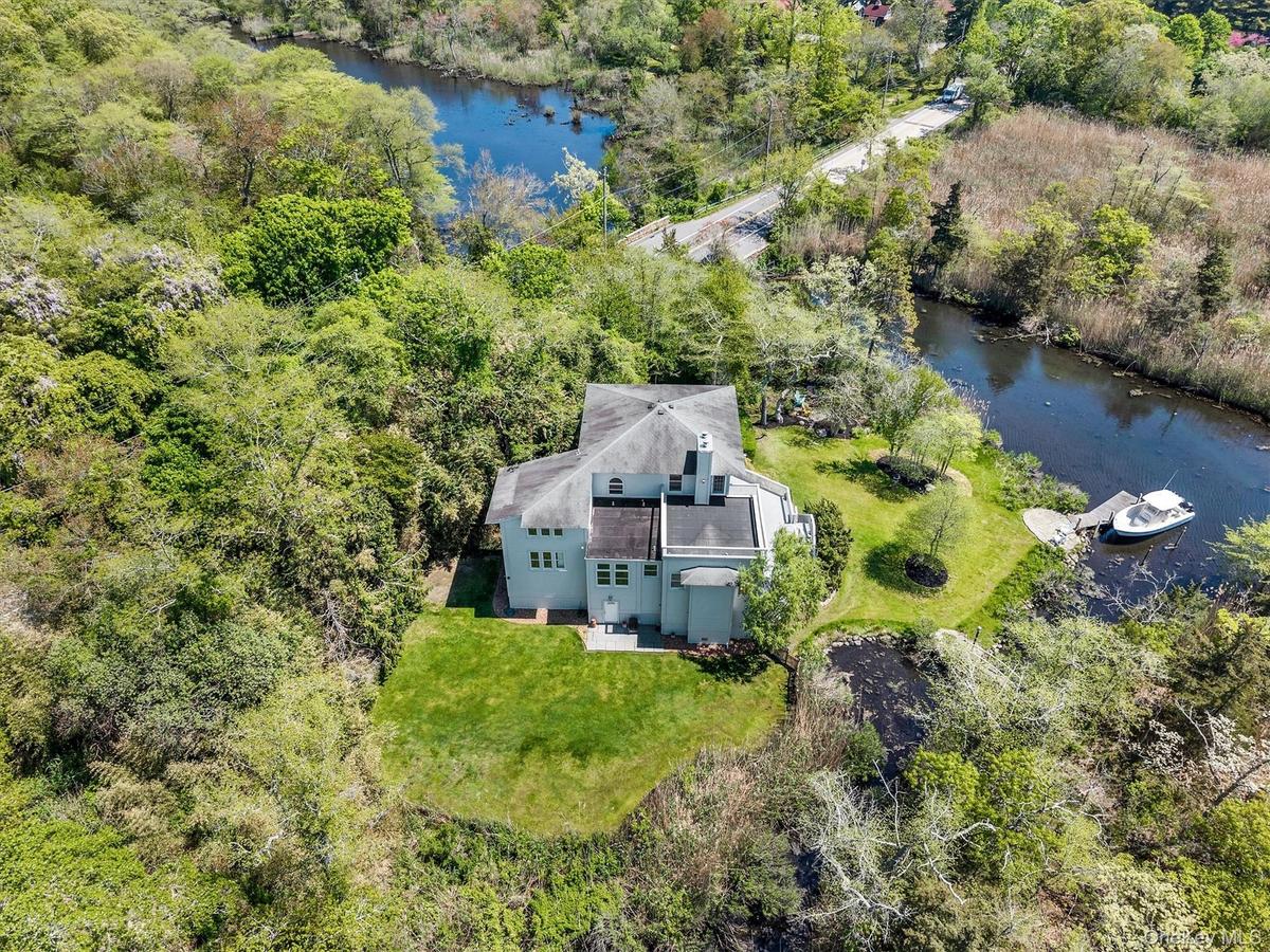 Waterfront property featuring a private boat dock, lush green lawns, mature trees, and a pond