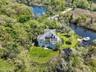 Waterfront property featuring a private boat dock, lush green lawns, mature trees, and a pond
