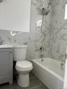 Bathroom with vanity, a combined bath / shower with marble appearance, and tile walls