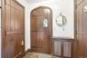 Arched wooden entry door with stained glass detail, complemented by dark wood paneling and stone tile flooring
