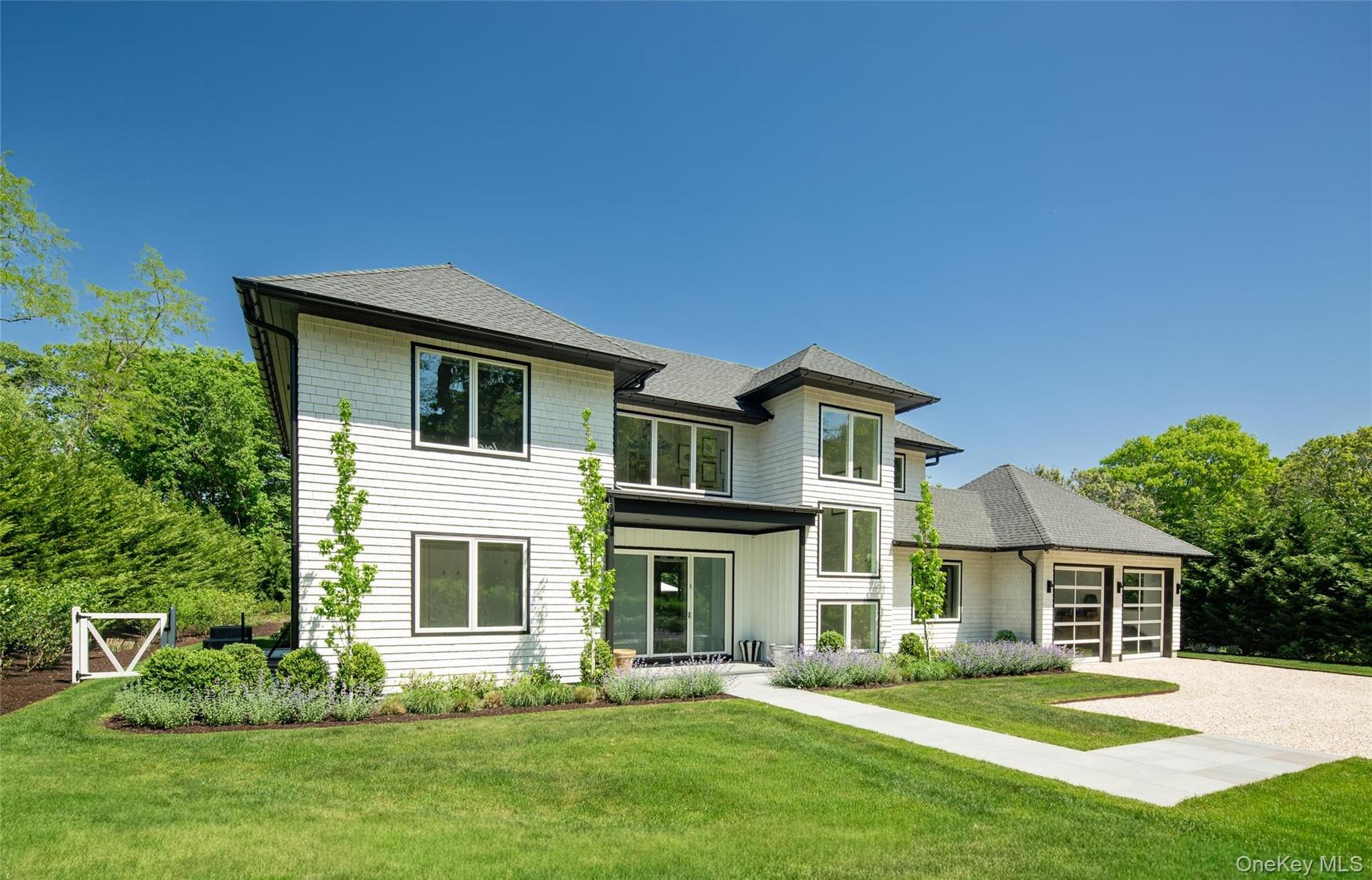 Contemporary residence featuring white shingle and horizontal siding, dark-trimmed windows, a multi-gabled roofline, a two-car garage with glass-panel