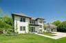 Contemporary residence featuring white shingle and horizontal siding, dark-trimmed windows, a multi-gabled roofline, a two-car garage with glass-panel