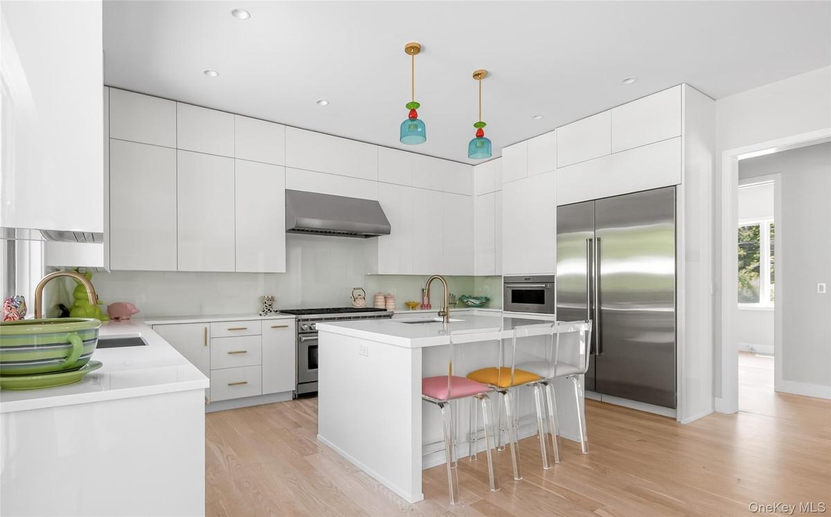 Bright kitchen featuring extensive white cabinetry, a central island with countertop seating, stainless steel appliances, light wood-finish flooring, 