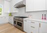 Gourmet kitchen featuring a stainless steel range with double ovens, coordinating hood vent, white cabinetry with gold-tone hardware, white countertop