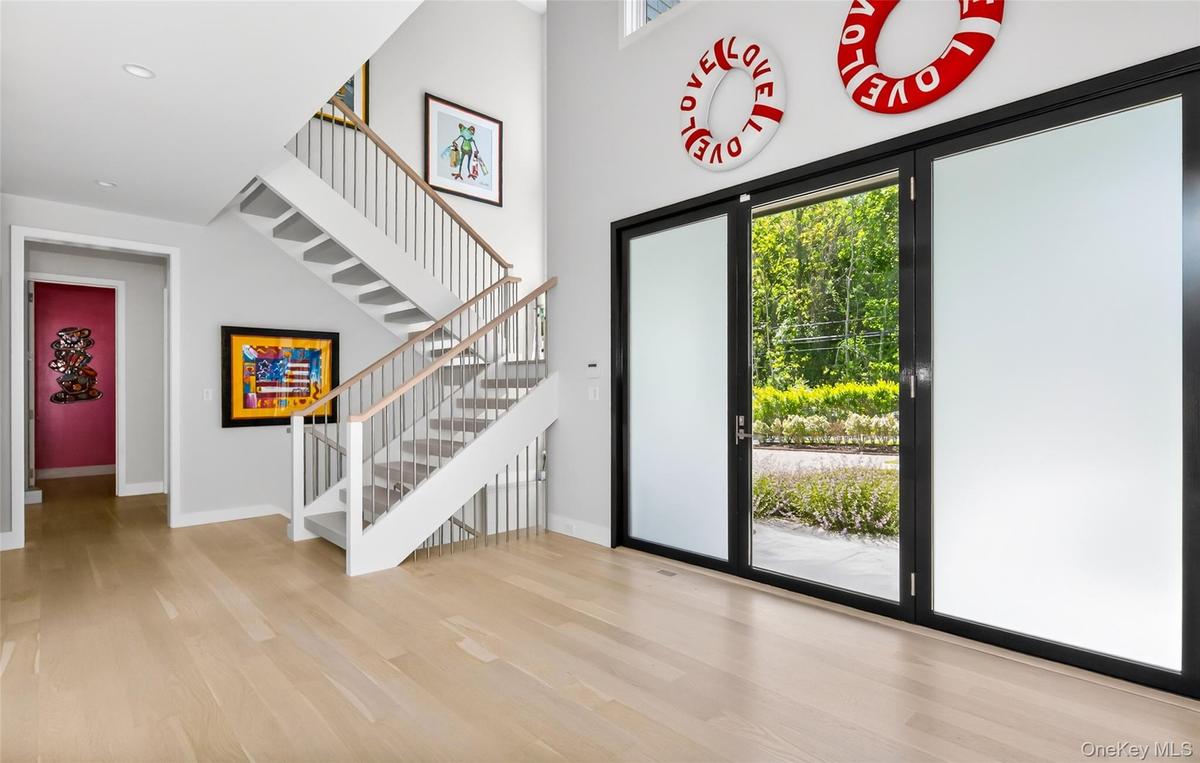 Grand entry featuring a light wood-finish flooring, a contemporary staircase with wood handrails and white risers, and tall ceilings