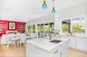 Open-concept kitchen featuring an island with an undermount sink, white cabinetry with brass hardware, and light wood-finish flooring