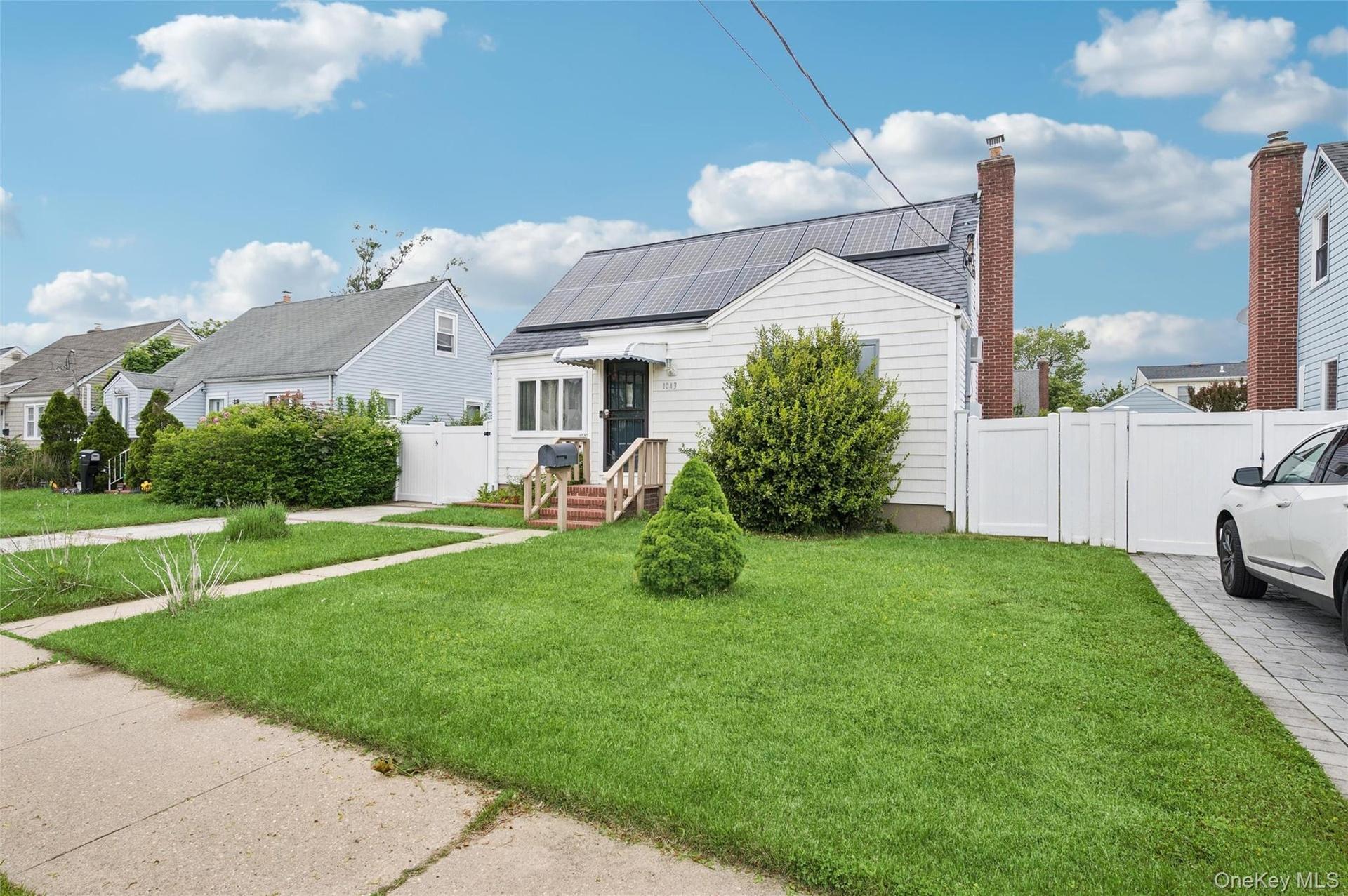 Cottage-style residence featuring white siding, a dark roofline with solar panels, and a white picket fence