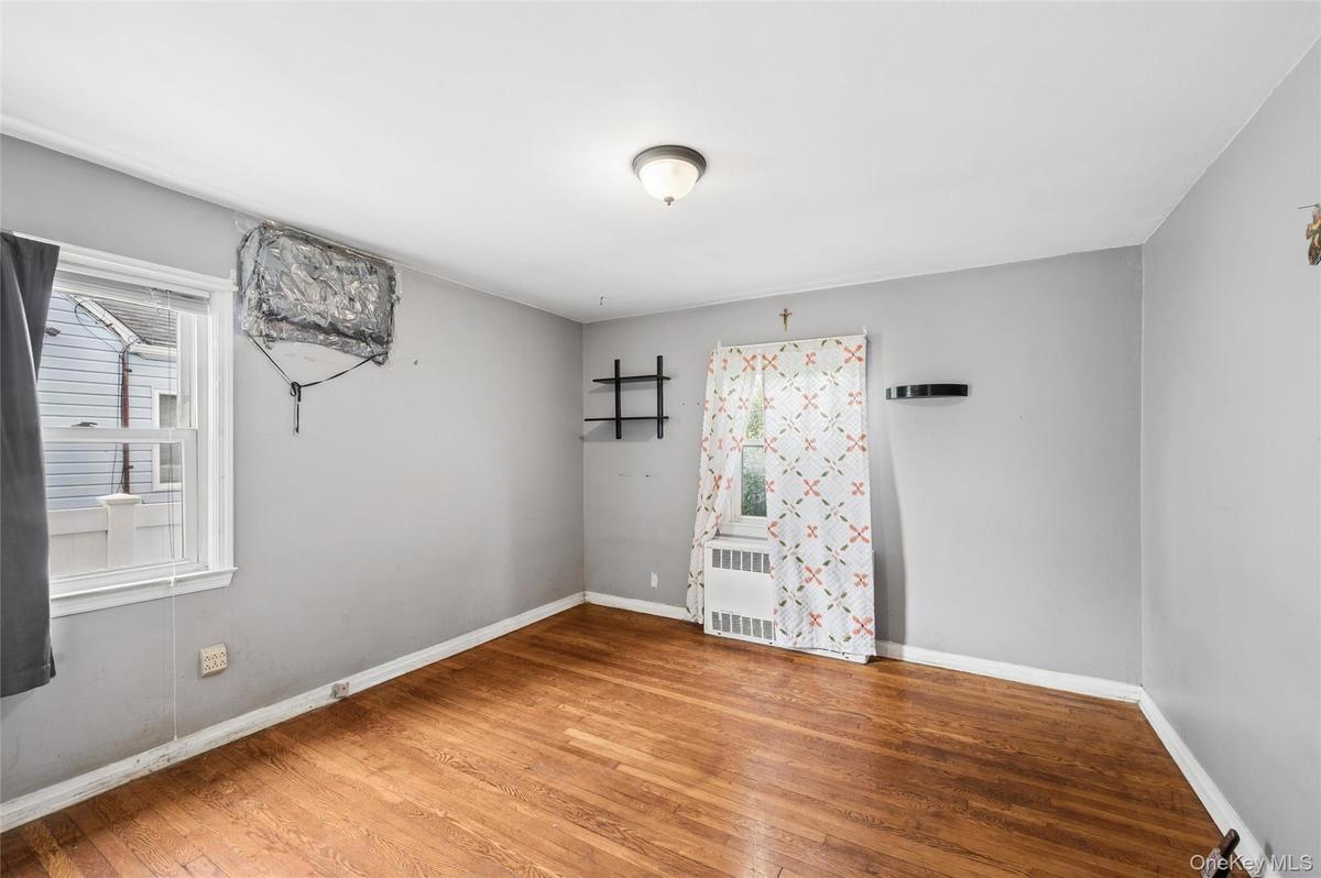 Hardwood flooring and light gray walls define this room, featuring a window-mounted air conditioning unit and baseboard heating