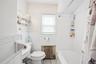 Bathroom featuring a white bathtub with a shower rod, a toilet, a window with blinds, and white wall tiling