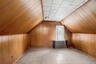Attic space featuring wood paneling on walls and ceiling, a window, and an exposed radiator