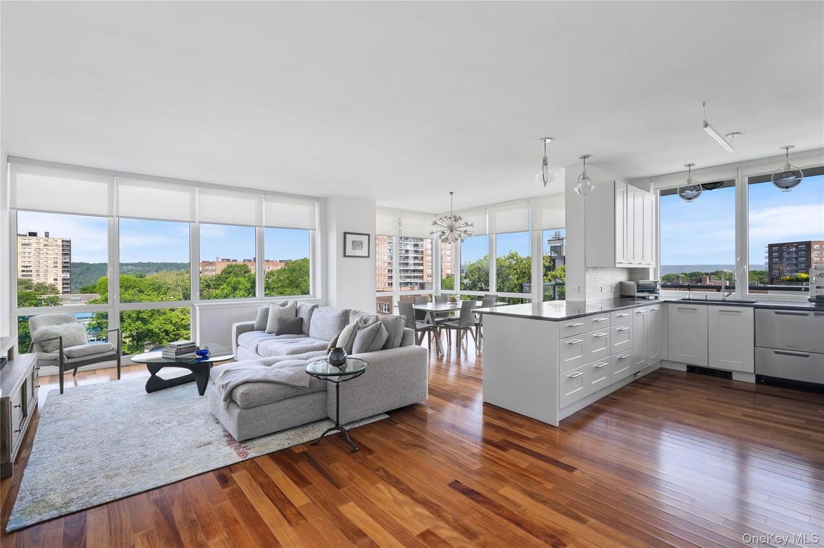 Open-concept living space with expansive wall-to-wall windows, wood-finish flooring, and a contemporary kitchen featuring white cabinetry and dark cou