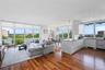 Open-concept living space with expansive wall-to-wall windows, wood-finish flooring, and a contemporary kitchen featuring white cabinetry and dark cou
