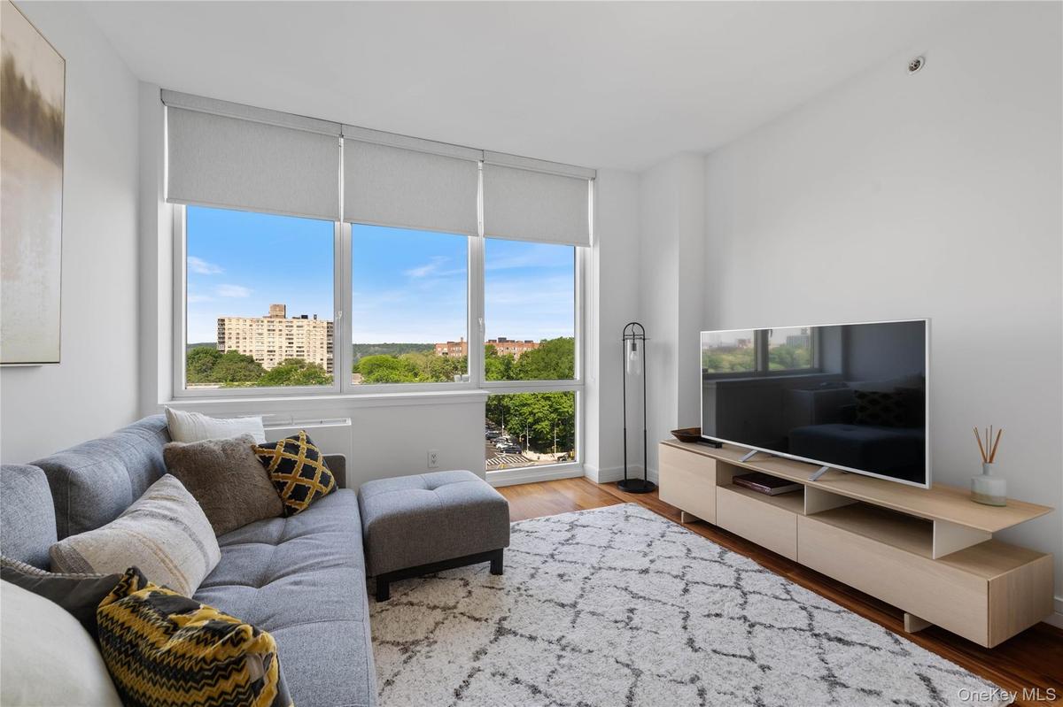 Expansive window wall with roller shades, hardwood flooring, recessed ceiling lighting, light wood-finish media console, and white walls