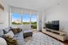 Expansive window wall with roller shades, hardwood flooring, recessed ceiling lighting, light wood-finish media console, and white walls