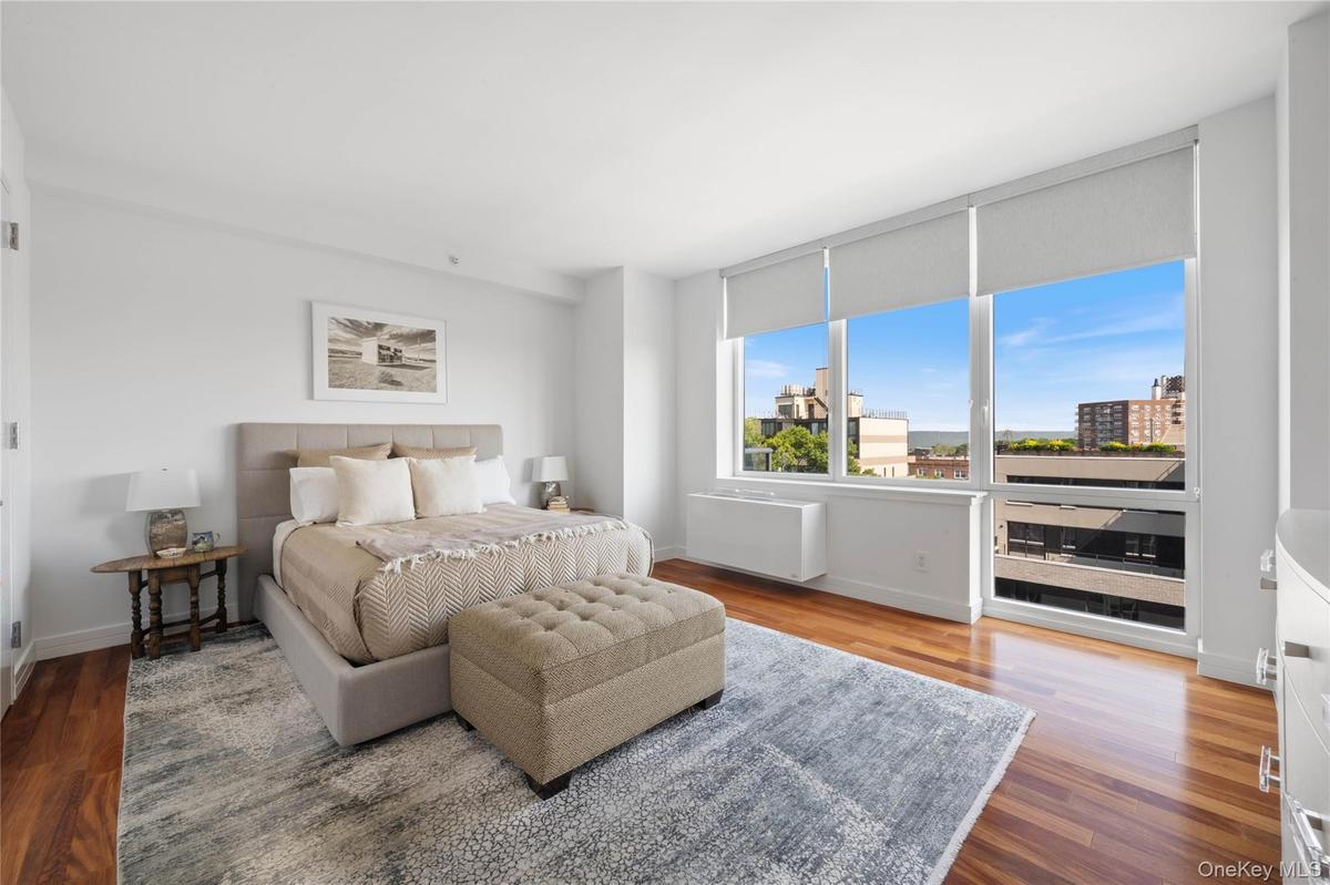 Bright room with extensive window system featuring roller shades, wood-finish flooring, and white walls