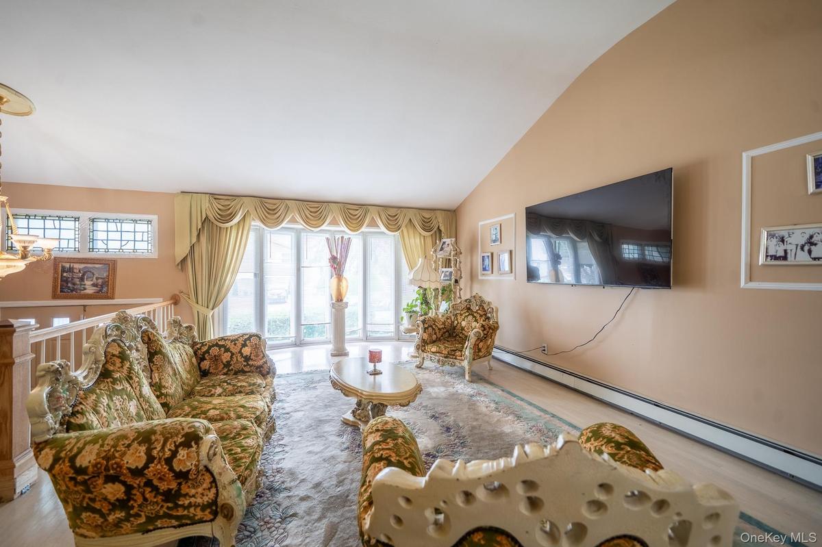 Living room with vaulted ceiling, healthy amount of natural light, baseboard heating, and wood finished floors