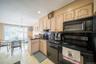 Kitchen with black appliances, light brown cabinets, a peninsula, dark countertops, and light wood finished floors